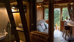 A wooden cabin interior with a bathroom, a cozy seating area with a sofa and pillows, and a dining space with a table and chairs. - Chalet Alpinka (Cerklje na Gorenjskem)