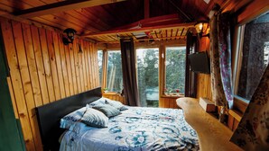 A wooden cabin bedroom with a bed, a nightstand, and a window with curtains. - Chalet Alpinka (Cerklje na Gorenjskem)
