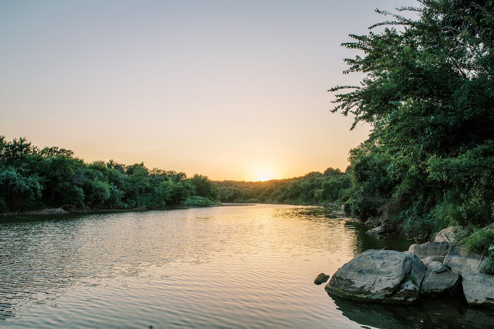 Un río con una superficie acuática tranquila, rodeado de exuberante vegetación y rocas.