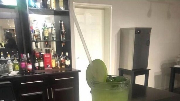 A bar area with a tall glass of green drink, a bottle, and a lime wedge on the counter.
