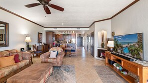 A spacious living room with a sofa, a coffee table, and a television. There is a kitchen in the background with cabinets and a dining area. - Sonoran Sky 708 A Wave From It All Charming Oceanfront (Puerto Peñasco)