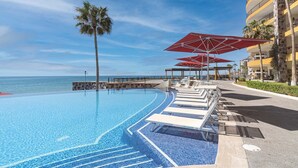 A pool area with lounge chairs and umbrellas, a palm tree, and a view of the ocean. - Sonoran Sky 708 A Wave From It All Charming Oceanfront (Puerto Peñasco)