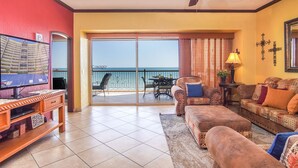 A living room with a television, a sofa, a chair, and a balcony with a view of the sea. - Sonoran Sky 708 A Wave From It All Charming Oceanfront (Puerto Peñasco)