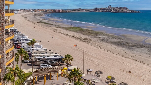 A beachfront hotel with RV parking, a pool, and beach umbrellas. - Sonoran Sky 708 A Wave From It All Charming Oceanfront (Puerto Peñasco)