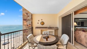 Een balkon met een ronde tafel, stoelen, een stenen muur en uitzicht op de oceaan.