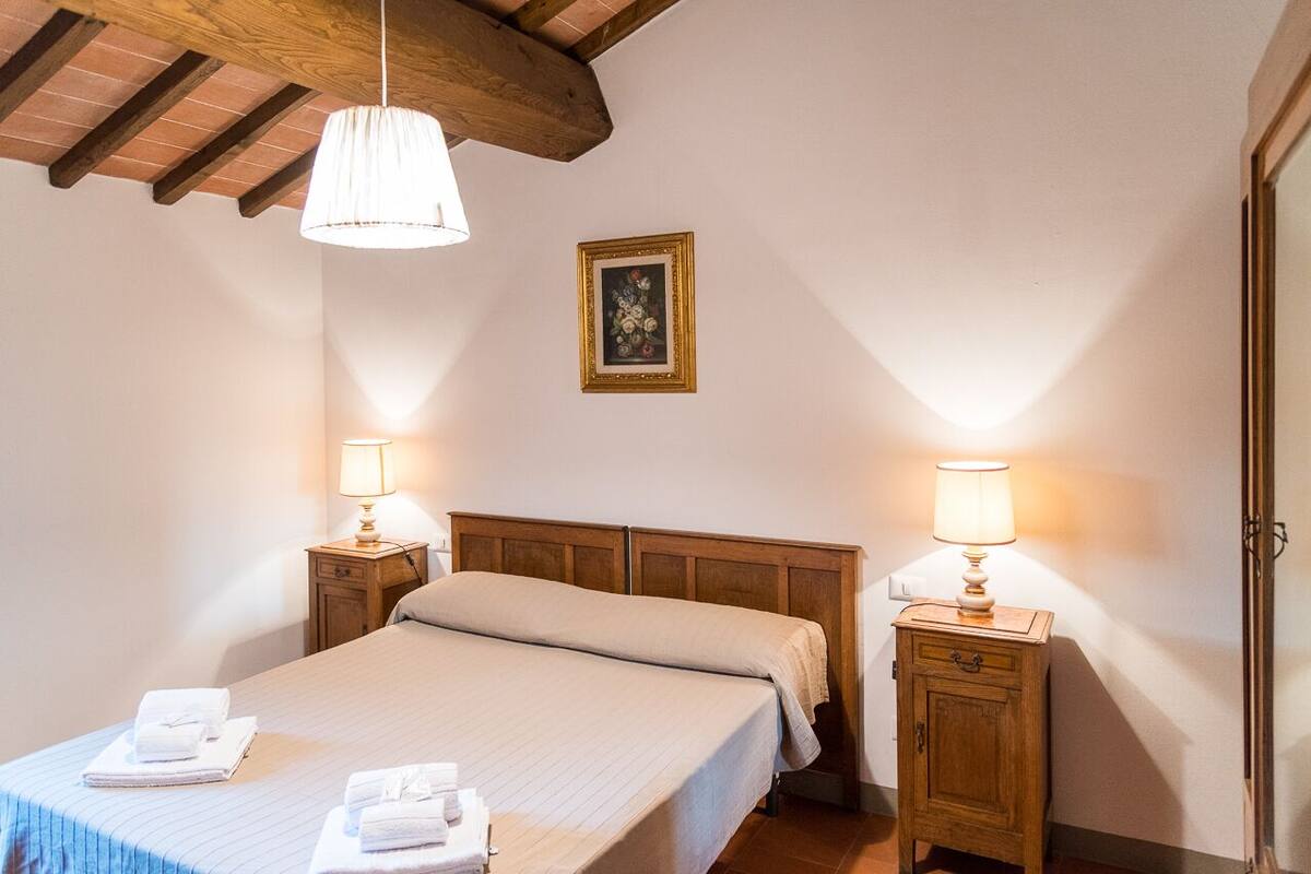Une chambre à coucher avec un lit, deux tables de chevet avec des lampes, une tête de lit en bois, un tableau encadré au mur et une porte sur le côté droit.