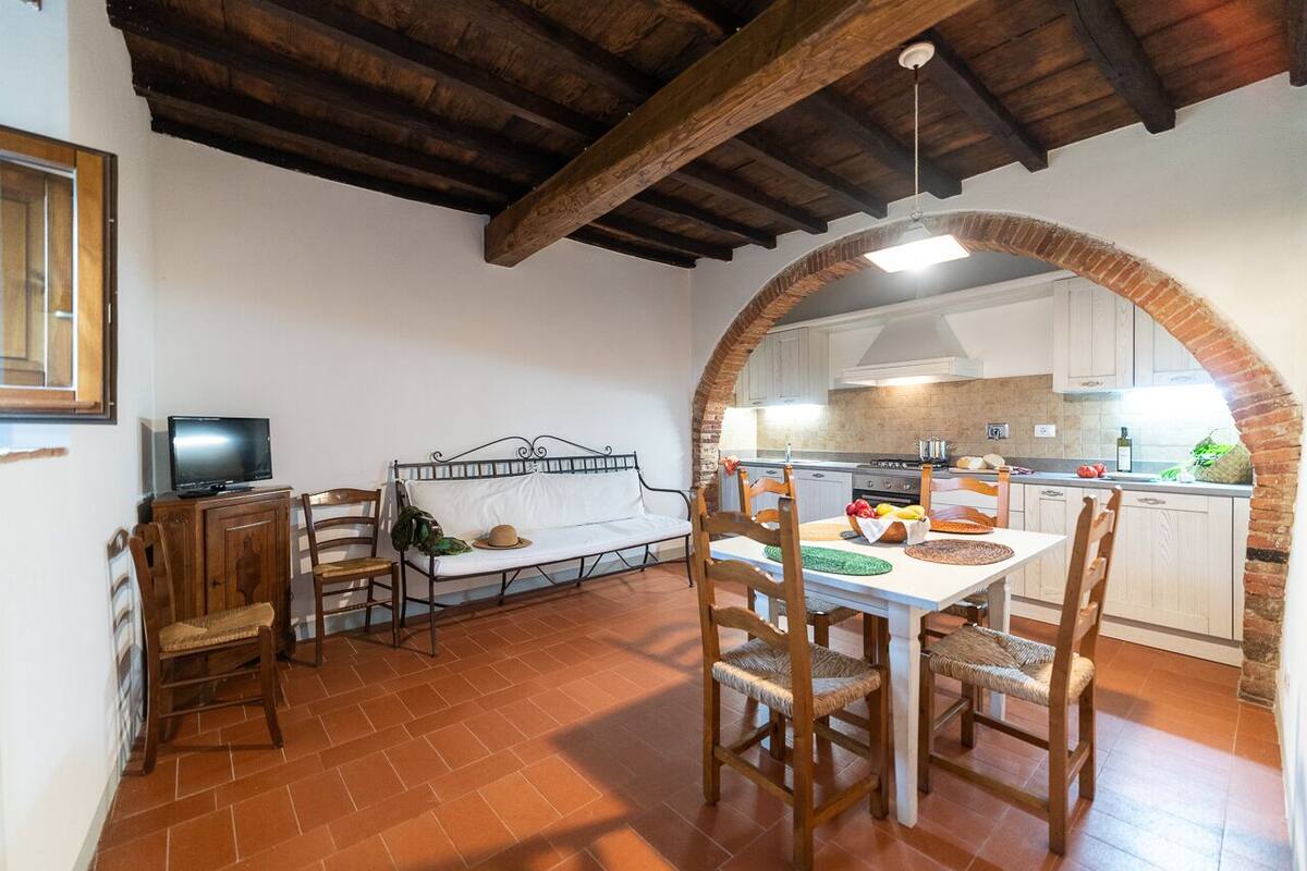 Un espace repas comprenant une table et des chaises, un téléviseur, et une cuisine visible à travers une arche.