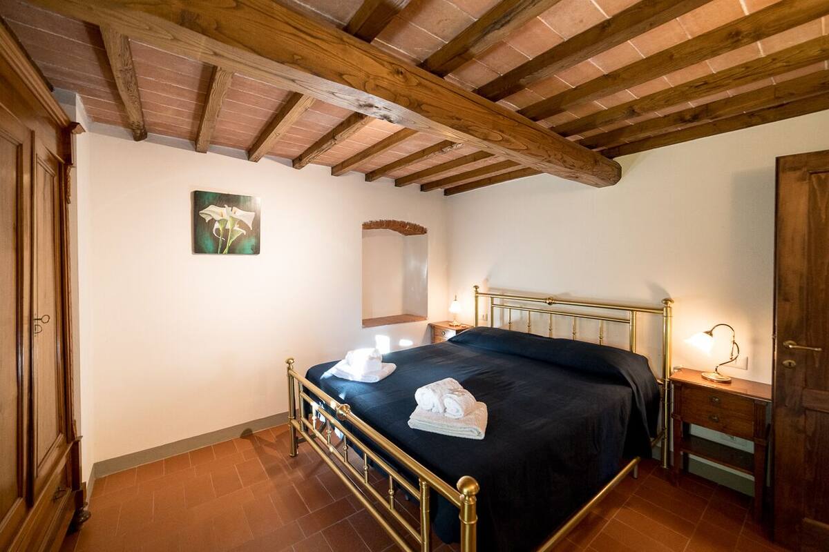 Une chambre à coucher avec un lit, des poutres en bois au plafond, une table de chevet, une lampe et un tableau au mur.