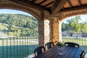 A covered outdoor seating area with a table and chairs, a brick wall, and a view of a hilly landscape. - Agriturismo Borgo Macereto (Dicomano)