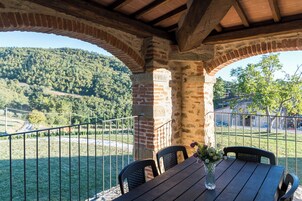 A covered outdoor seating area with a table and chairs, a brick wall, and a view of a hilly landscape.
