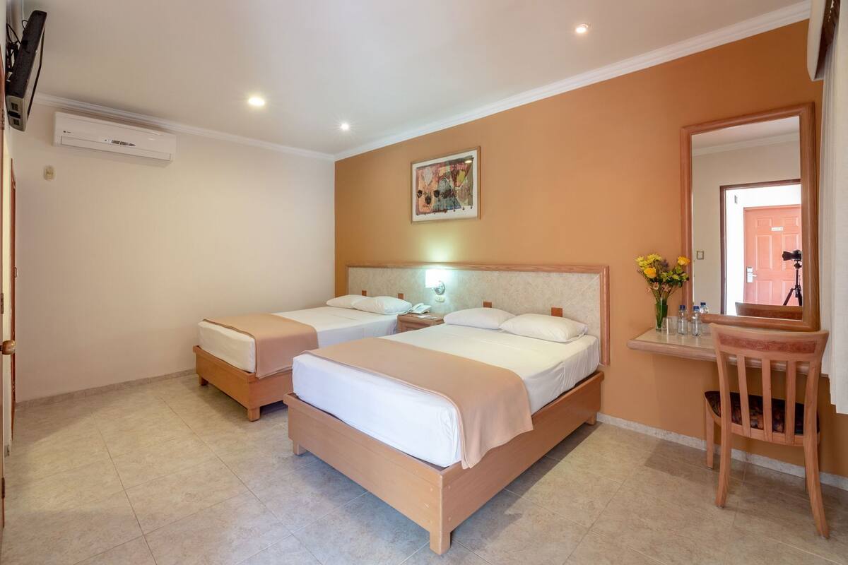 A hotel room with two beds, a desk with a chair, a mirror, and a painting on the wall.