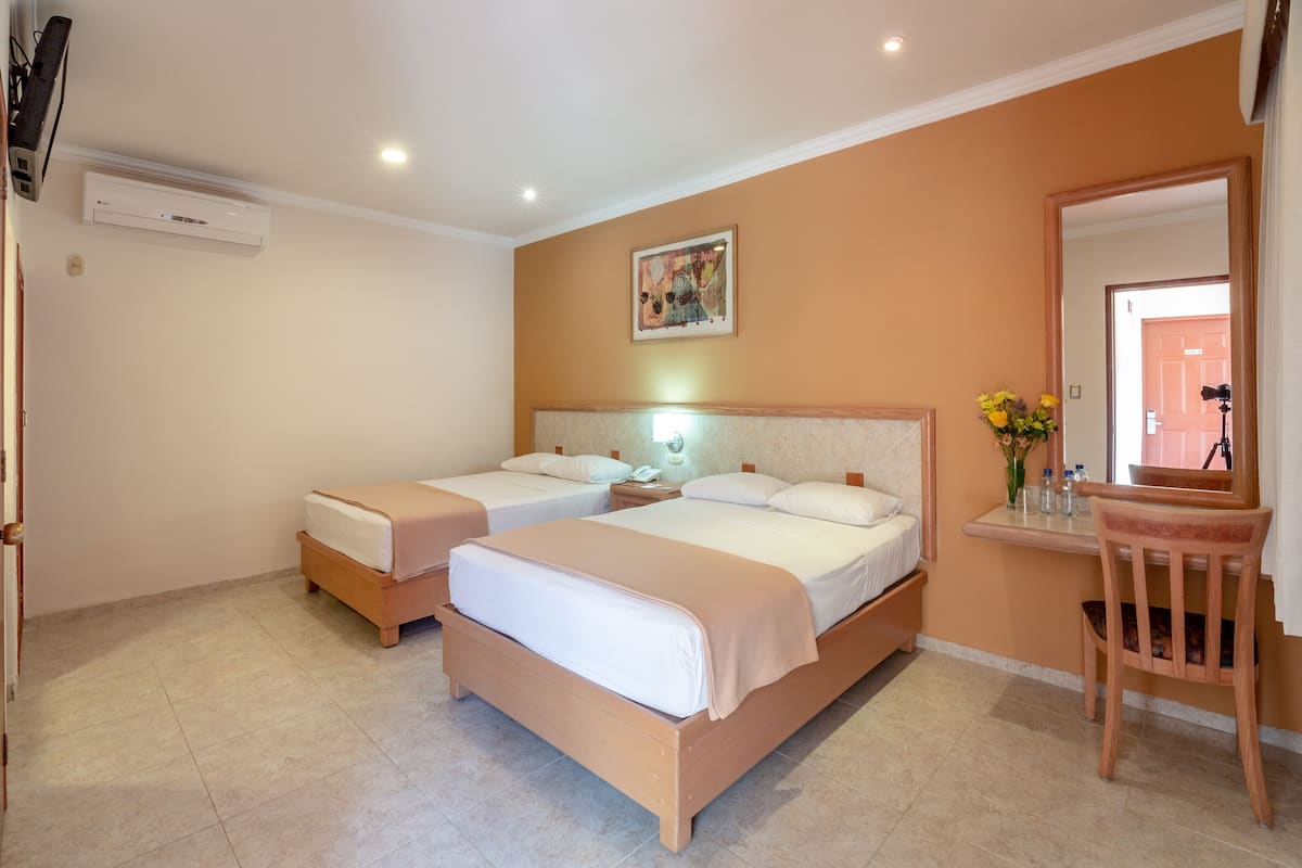 A hotel room with two single beds, a desk with a chair, a mirror, and an air conditioning unit.