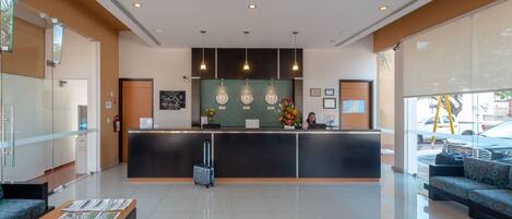 A modern reception area with a black counter, glass doors, and a seating area with patterned cushions.