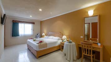 A hotel room with a bed, bedside table, lamp, chair, and a mirror.