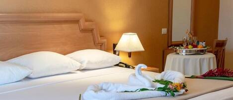 A hotel room with a bed, pillows, a bedside lamp, a table with a vase of flowers, and a mirror on the wall.