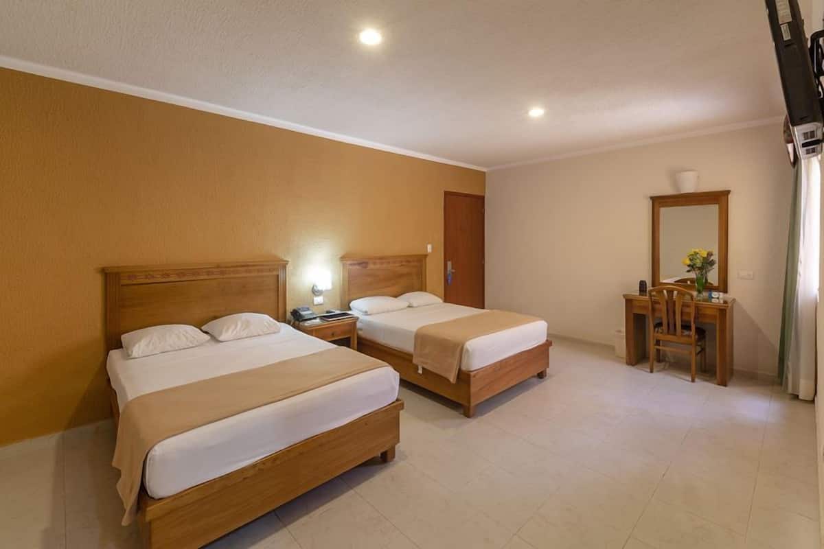 A hotel room with two wooden beds, a desk with a chair, and a mirror.