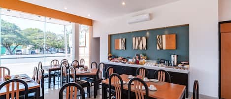 Un restaurante con varias mesas y sillas, una barra de cocina con distintos objetos y vistas a la calle.