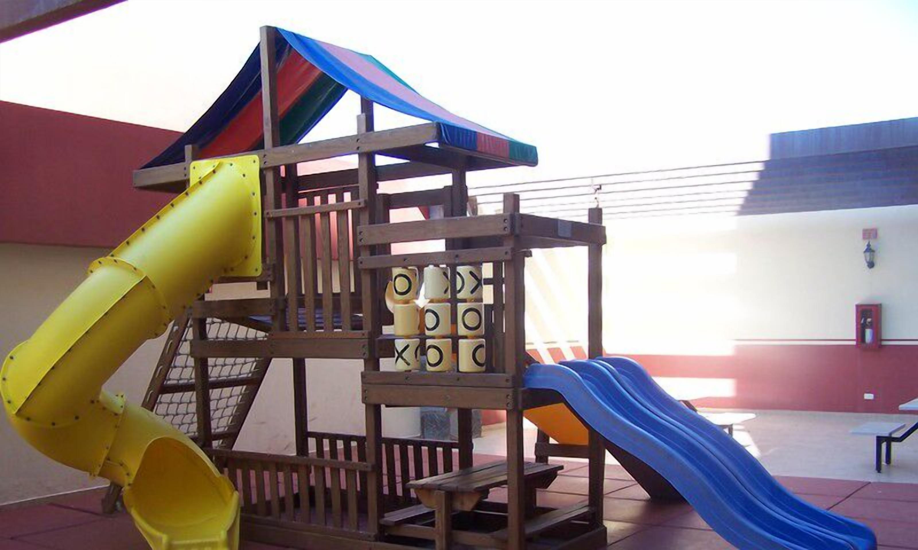 Un parque infantil con tobogán, zona de escalada y un tobogán tubular amarillo.