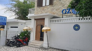 Ein Hostel namens 'OZORA' mit einer Stein-Fassade, einer Holztür und einer weißen Wand mit einem blauen Emblem. Vor dem Gebäude stehen zwei Regenschirme und ein Motorrad.
