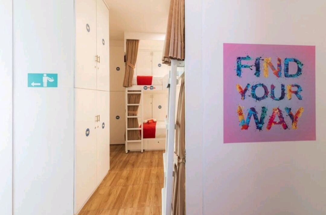 Une chambre d’hôtel avec un lit superposé, une armoire, un petit bureau et un panneau indiquant « Comment vous orienter » sur le mur.