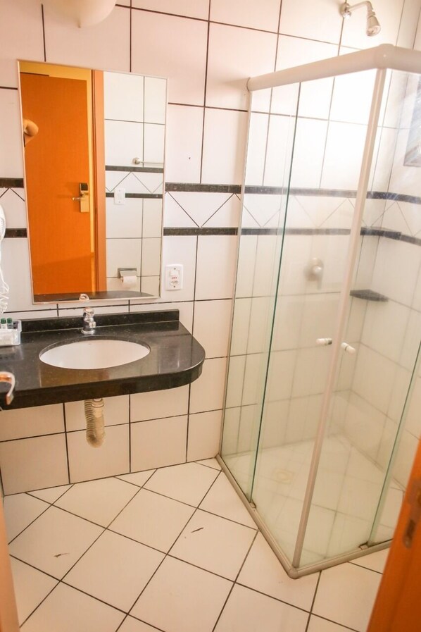 A bathroom with a glass-enclosed shower, a sink with a mirror, and tiled walls.