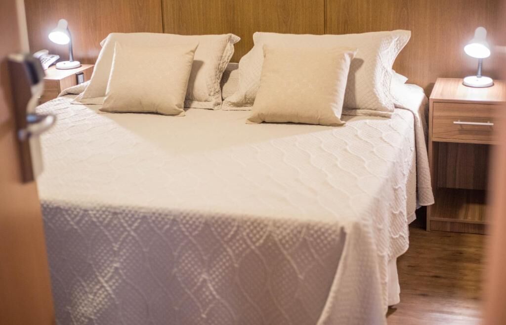 A neatly made bed with a white bedspread and pillows, a wooden headboard, and bedside lamps.