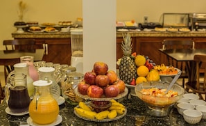 A breakfast buffet with various fruits, a pitcher of orange juice, and a bowl of cereal.