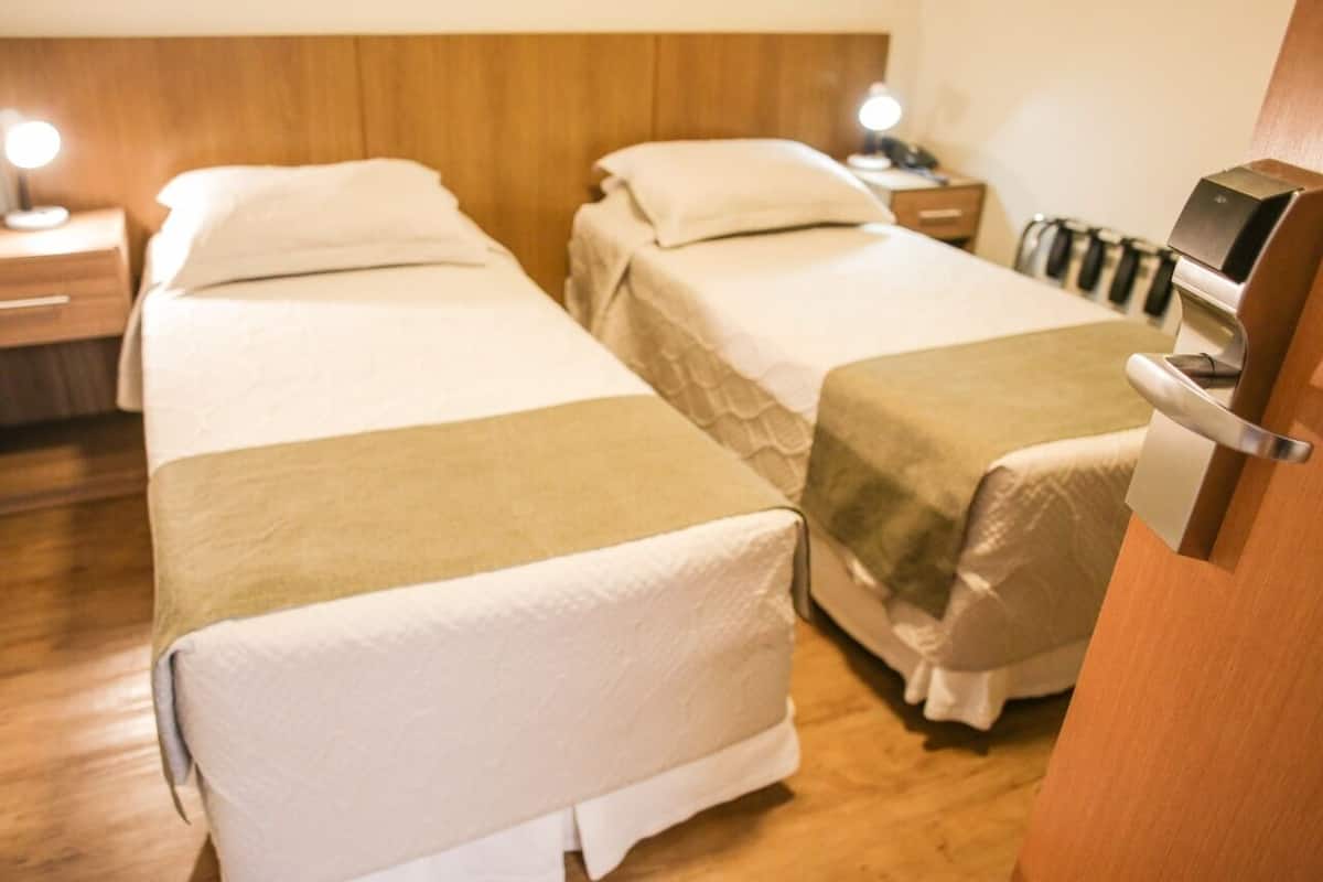 Une chambre d’hôtel avec deux lits simples, des têtes de lit en bois, des lampes de chevet et un mini-bar.