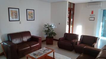 A living room with a brown leather sofa, a wooden coffee table with newspapers, and a potted plant.