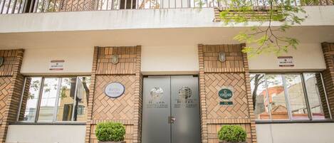 Entrada de hotel con puertas dobles, dos macetas pequeñas y un banco al exterior.