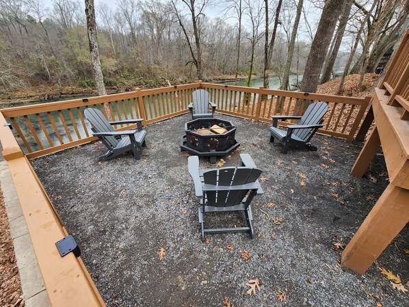 Une terrasse dotée de chaises Adirondack et d’un foyer, entourée d’une rambarde en bois et d’un sol en gravier.