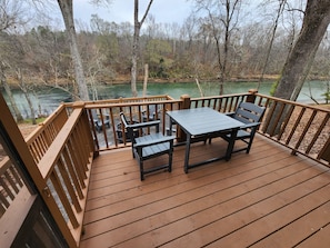 Une terrasse en bois avec une table et des chaises, donnant sur un lac entouré d’arbres.