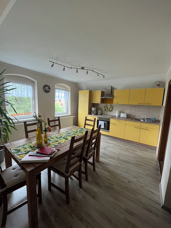 Un coin repas avec une table et des chaises en bois, une cuisine avec des placards jaunes et une fenêtre donnant sur un paysage verdoyant.