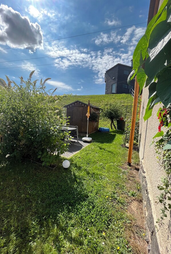 Un patio trasero con un cobertizo de madera, un pequeño jardín y una casa al fondo.