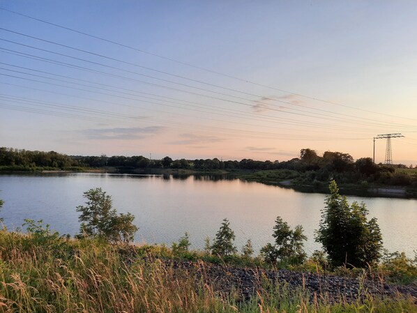 A calm lake with a stone wall in the foreground and a power line tower in the background. - Vacation Apartment Near the Upper Reservoir (Oberwartha)