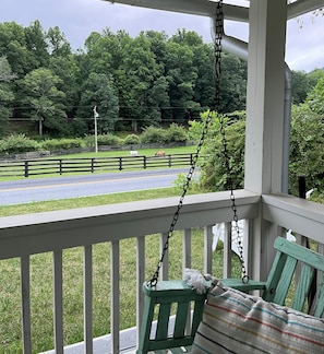 Une véranda avec une chaise suspendue et une vue sur un pré clôturé où paissent des chevaux.