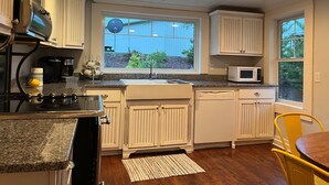 Ett kök med vita skåp, en bänkskiva i granit, en inbyggd mikrovågsugn och ett fönster med utsikt över grönområden utanför.