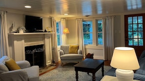 Ett vardagsrum med en öppen spis, en tv, en soffa, en fåtölj och en lampa.