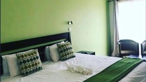 Ein Hotelzimmer mit Bett, Kissen, einer grünen Tagesdecke und einem Fenster mit Vorhängen.