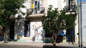 A building with a mural of a tree on the facade, a balcony with a metal railing, and a tree in front of the building. - FABULOSO BUENOS AIRES  ONE (Ground floor Balvanera)