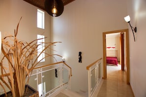 A staircase with a railing, a potted plant, a wall-mounted light fixture, and a doorway leading to a room with a bed.