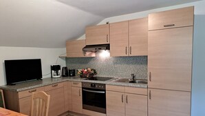 Una cocina compacta con armarios de madera, horno empotrado, lavamanos y televisor.