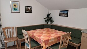 Comedor con una mesa cubierta con mantel a cuadros, rodeado de sillas de madera y un banco con cojín verde.