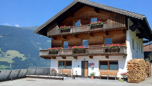 Un edificio de madera de dos pisos con balcones, un banco de madera afuera y vistas a la montaña.