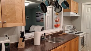 A kitchen with wooden cabinets, a stainless steel sink, a microwave, and hanging pots. - Sweet downtown home! (St. John's)
