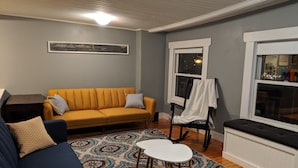 A living room with a yellow sofa, a blue couch, a patterned rug, a small white table, and a window with a view of the city. - Sweet downtown home! (St. John's)