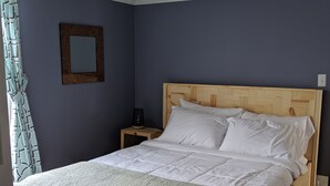 A bedroom with a wooden bed, white bedding, a nightstand with a lamp, and a mirror on the wall. - Sweet downtown home! (St. John's)