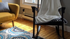 A room with a window, a yellow armchair, a patterned rug, and a black chair with a white cover. - Sweet downtown home! (St. John's)