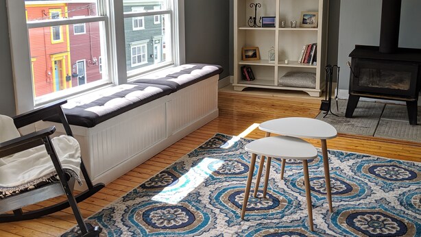 A cozy living room with a rocking chair, a white radiator, a bookshelf, and a fireplace. - Sweet downtown home! (St. John's)