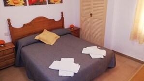Una cama bien hecha con cabecera de madera, una mesita de noche con lámpara y un armario con puertas empaneladas.